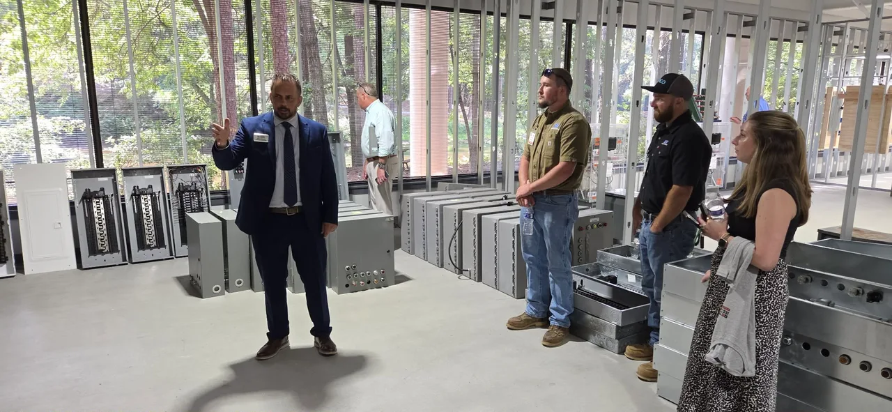 A tour group inside an electrical training room, surrounded by practice panels and wiring stations.